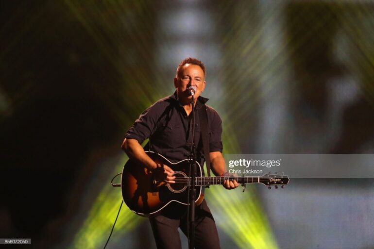 A man with a guitar on stage in front of lights.