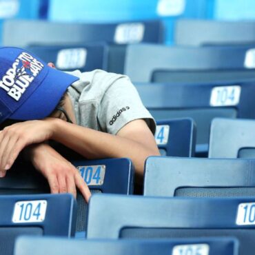 A man in blue baseball cap sleeping on top of seats.