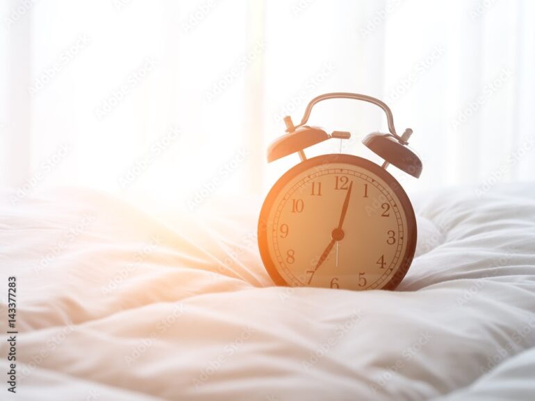 A clock sitting on top of a bed in the sunlight.